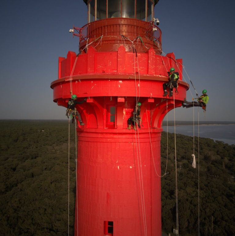Cordistes suspendus autour de la galerie rouge d'un phare